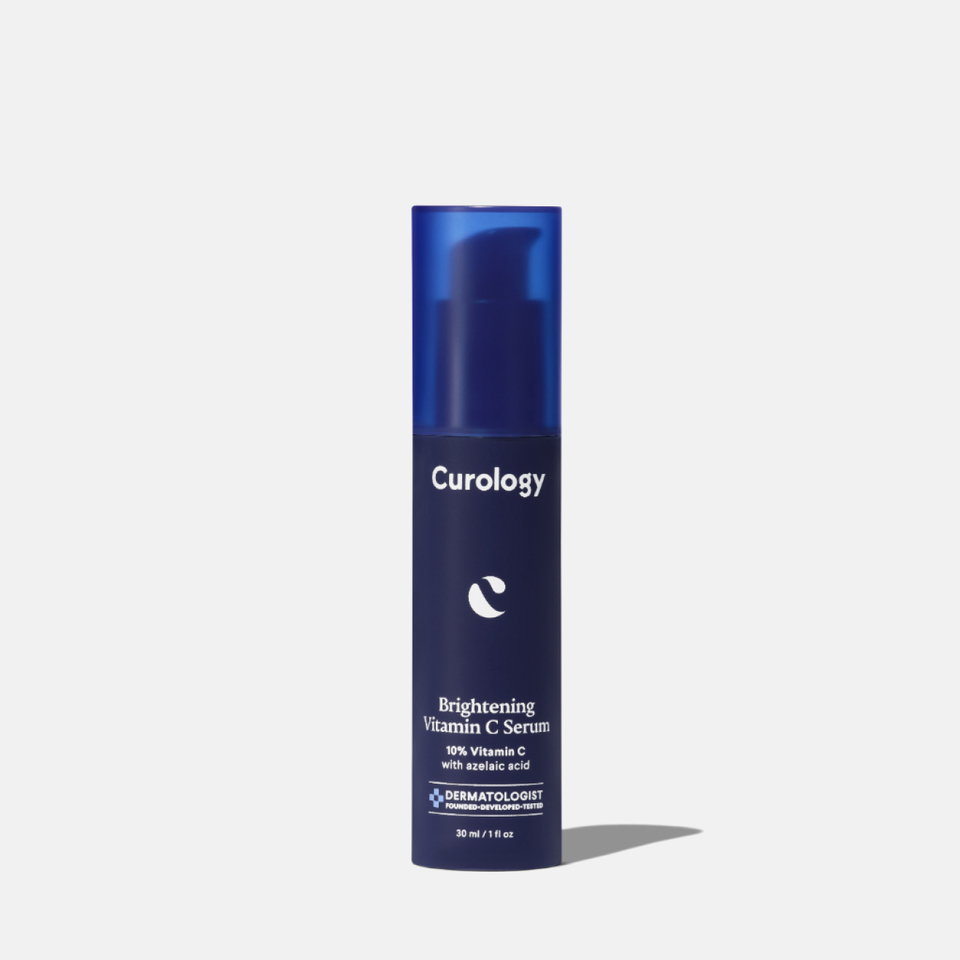 Curology Brightening Vitamin C Serum in a tall dark blue pump bottle, labeled ‘10% Vitamin C with azelaic acid,’ dermatologist founded, developed, and tested.