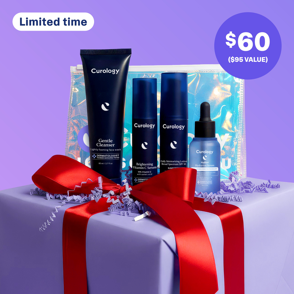 A set of four Curology products standing in front of a Holiday-exclusive Holographic Gift Bag on top of a box wrapped in purple paper with red ribbon against a purple background. The products included are the Gentle Cleanser, Hydro+ Hydration Serum, Brightening Vitamin C Serum, and Daily Moisturizing Lotion Broad Spectrum SPF 30.